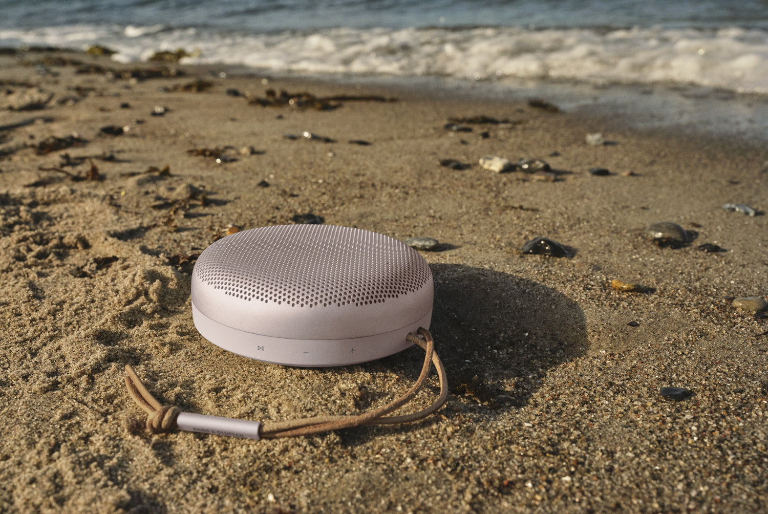 BeoSound A1 in pink im Sand an einem Strand - BeoSound A1 ist staubdicht