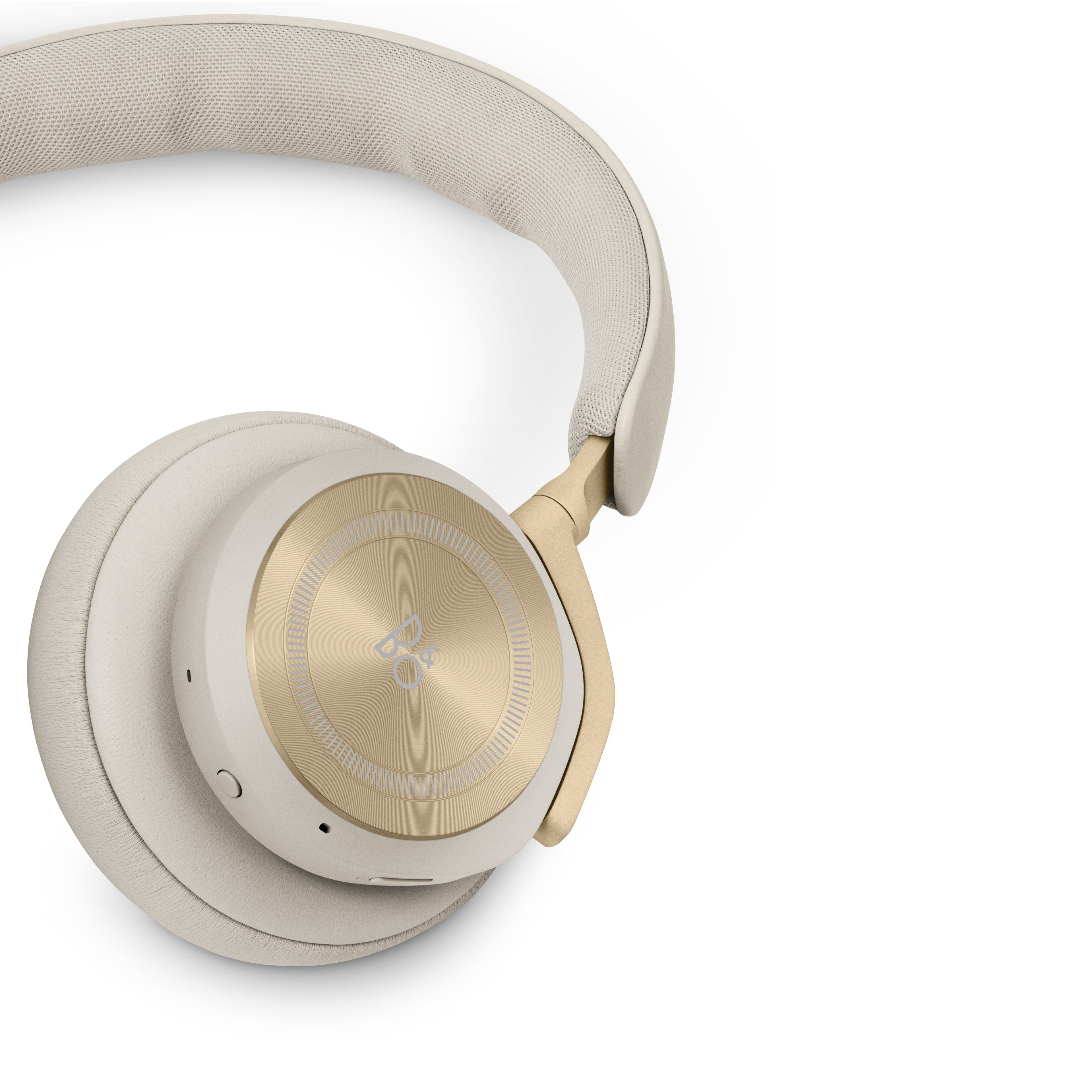 Nahaufnahme der rechten Ohrmuschel der Beoplay HX. Der Fokus liegt auf der präzisen Aluminium-Verarbeitung des Touch-Interface und dem Übergang zum sandfarbenen Textil-Kopfband.