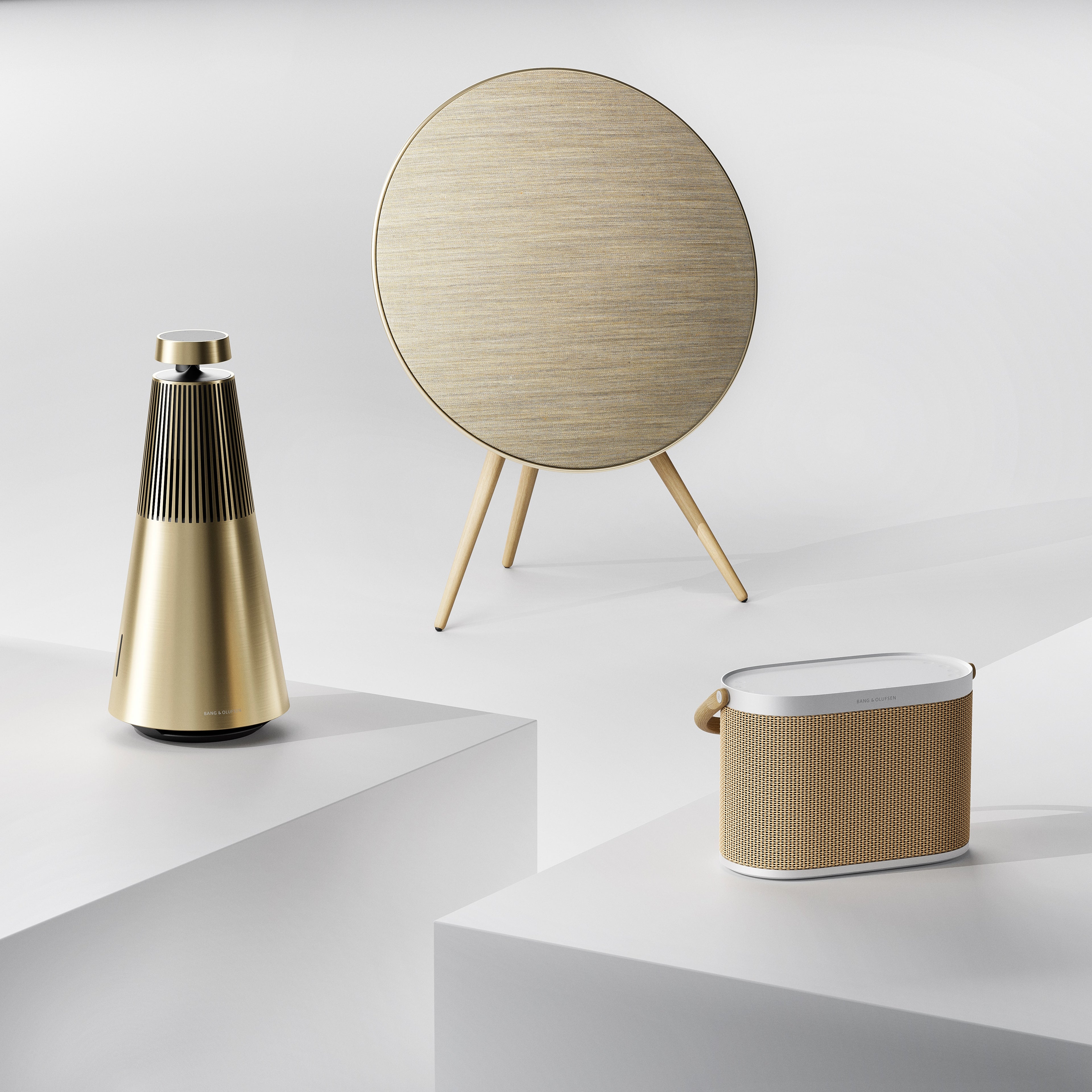 Minimalistisches Studio-Arrangement der Bang & Olufsen Gold Tone Serie. Gezeigt werden die Beosound 2, die Beosound A9 und die Beosound A5 in einer harmonischen Kombination aus goldfarbenem Aluminium, hellem Eichenholz und hochwertigen Textilien. Ein Symbol für vernetzten High-End-Klang im ganzen Haus (Multiroom).