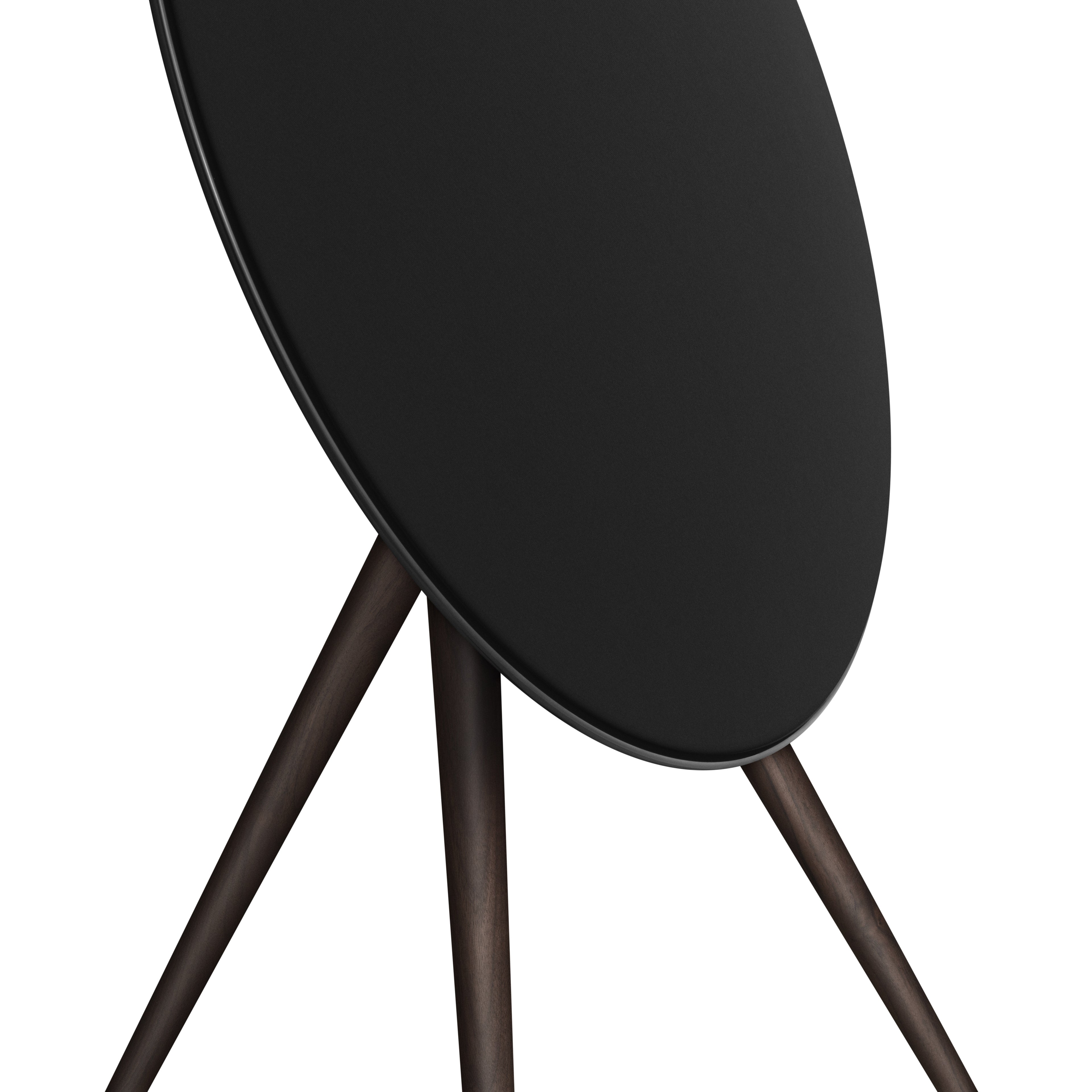 Detaillierte Nahaufnahme der Bang & Olufsen Beosound A9 in Black Anthracite. Der Fokus liegt auf dem Übergang zwischen dem anthrazitfarbenen Aluminiumring, der fein gewebten schwarzen Textilfront und den Beinen aus massiv dunklem Nussbaumholz. Die Aufnahme betont die edle Haptik und die erstklassige Materialverarbeitung.